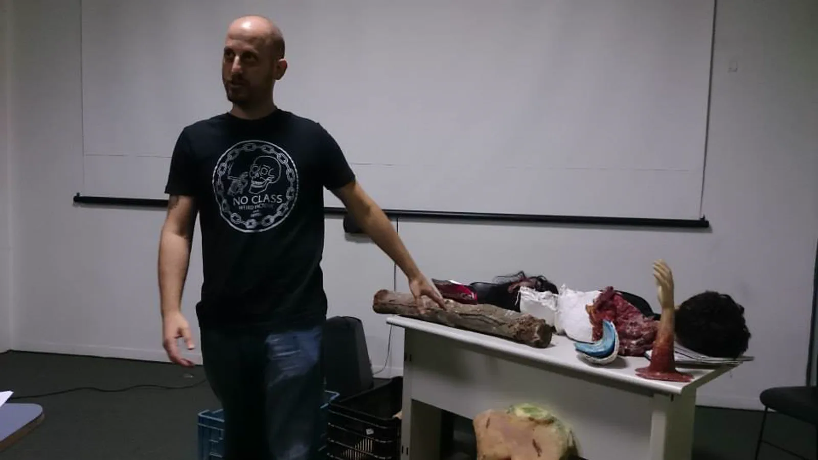 Instrutor apresentando peças cênicas de membros humanos sobre a mesa de trabalho