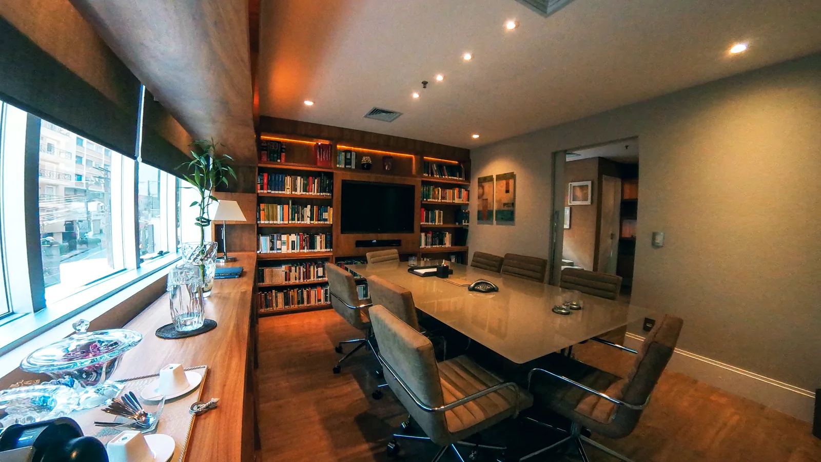 Sala de reunião com mesa longa, cadeiras de couro e parede de estantes ao fundo