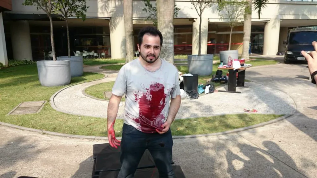 Participante de camisa branca após o disparo de uma carga de tiro cênico com sangue no peito