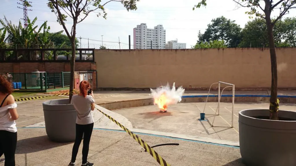 Estouro branco de uma carga explosiva no pátio, com uma participante observando ao lado