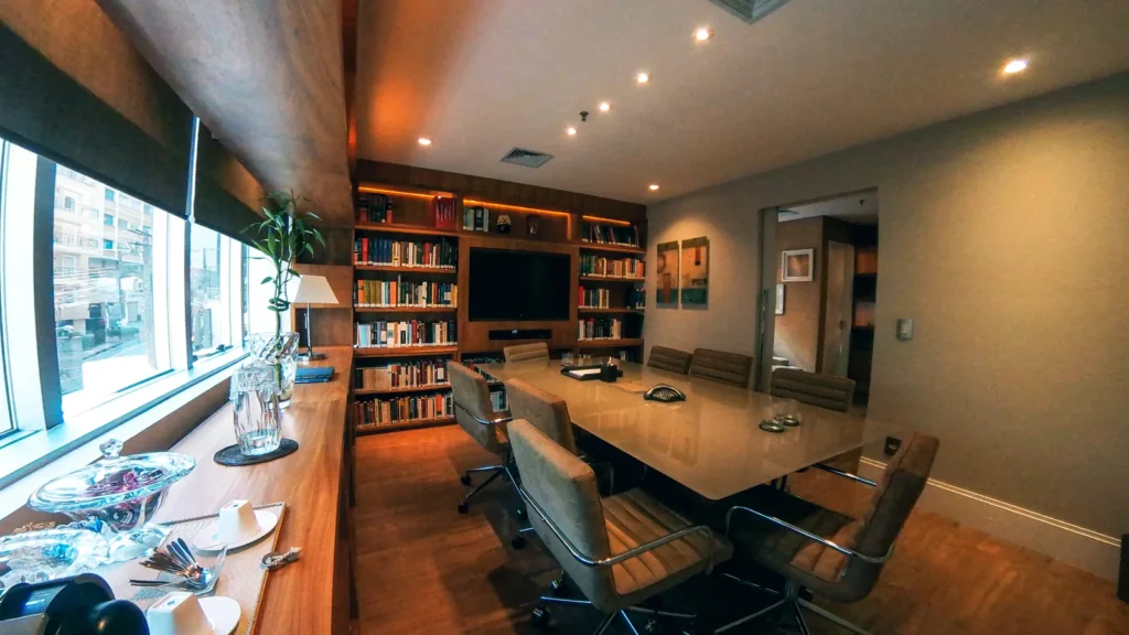 Sala de reunião com mesa longa, cadeiras de couro e parede de estantes ao fundo
